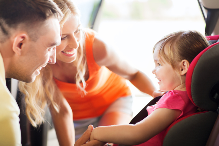 family, transport, safety, road trip and people concept - happy parents talking to little girl in baby car seat